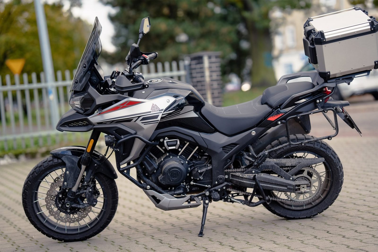 Czarny motocykl turystyczny z kufrem zaparkowany na chodniku