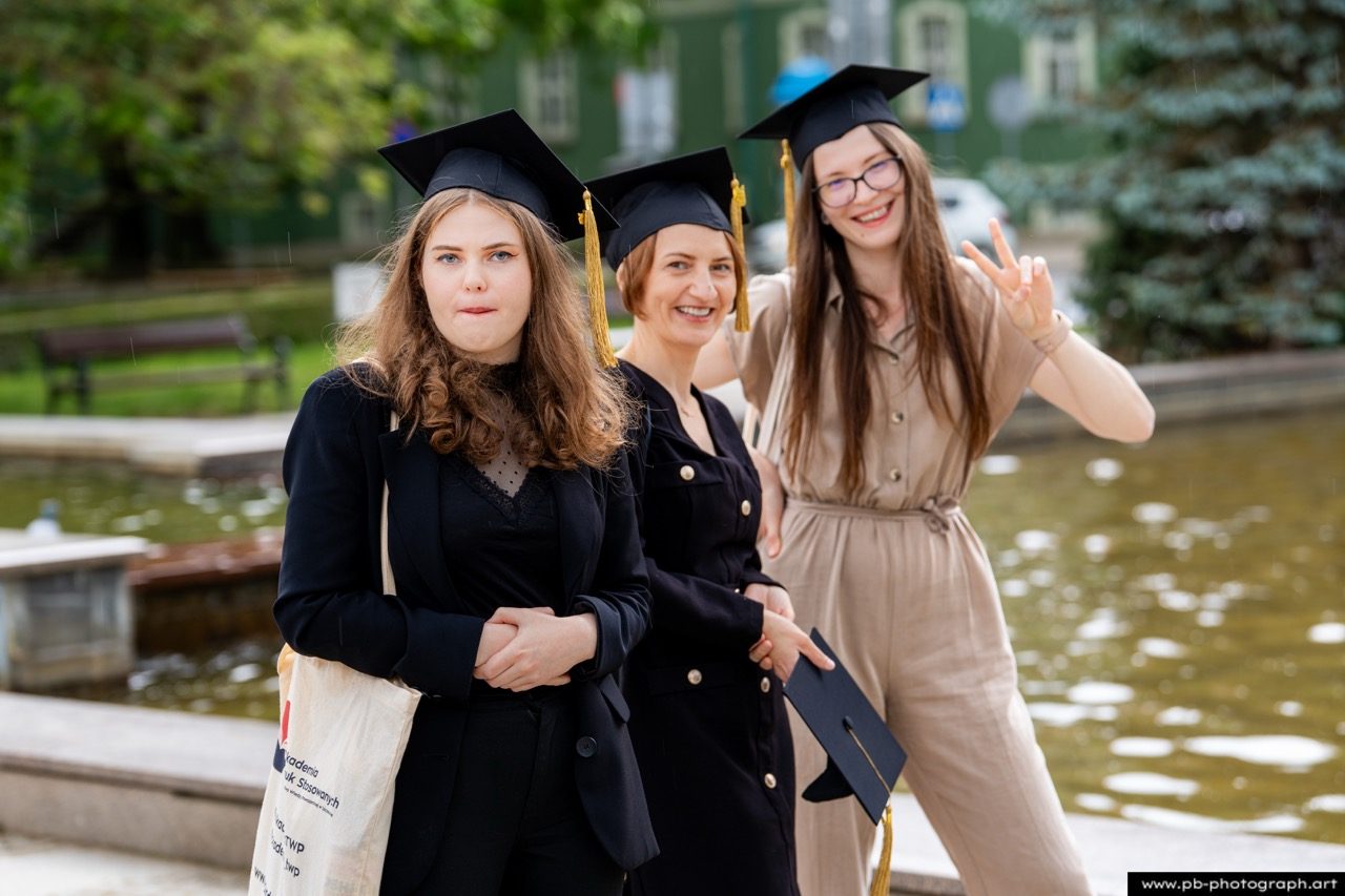 Trzy osoby w togach przy fontannie, uśmiechnięte.