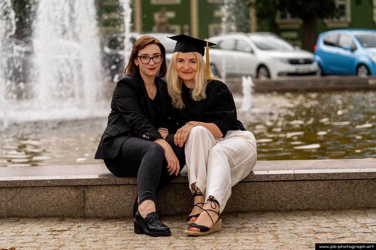 Dwie osoby siedzące przy fontannie, jedna w todze.