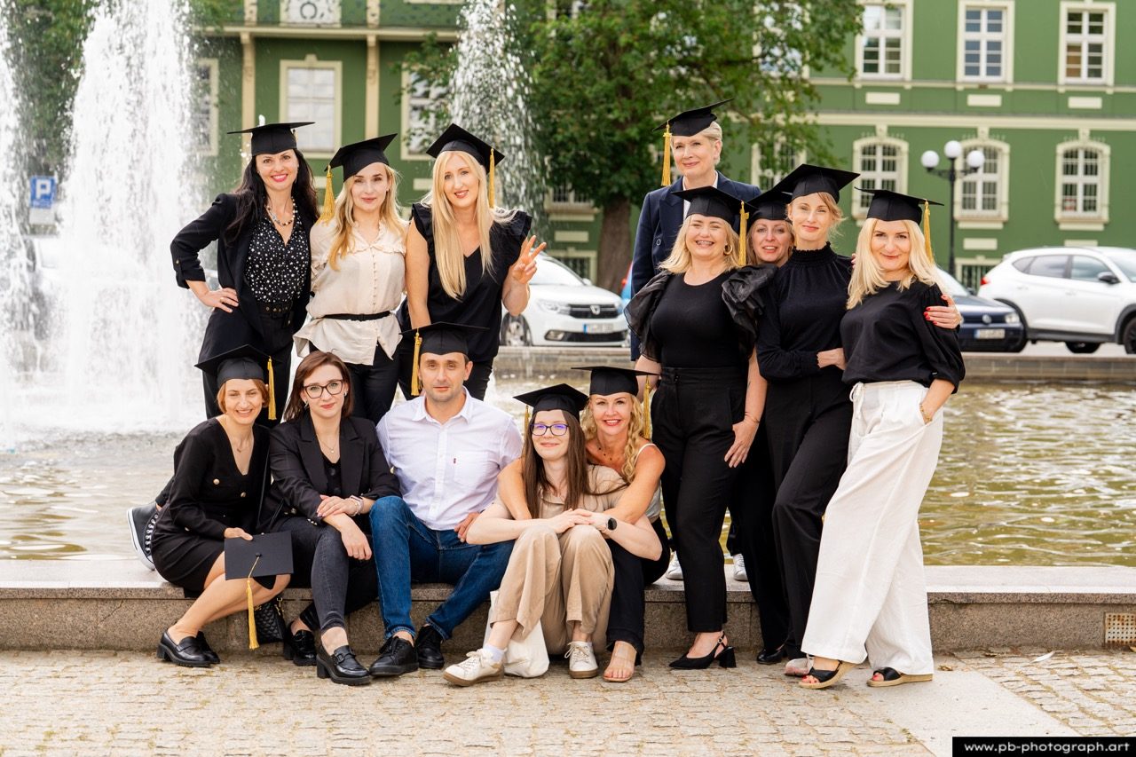 Grupa absolwentów w togach przy fontannie.