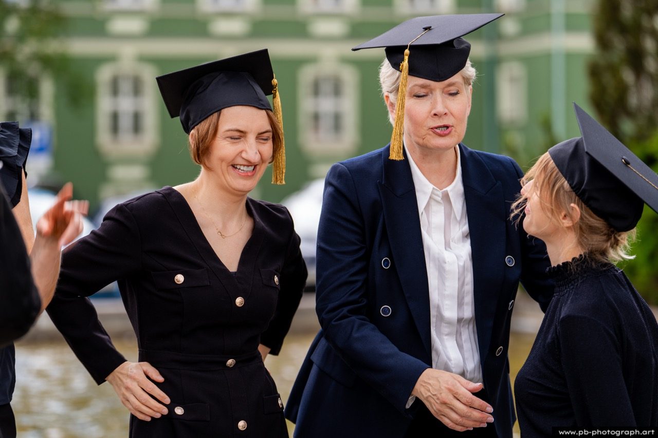 Dwie osoby w togach rozmawiające i śmiejące się.