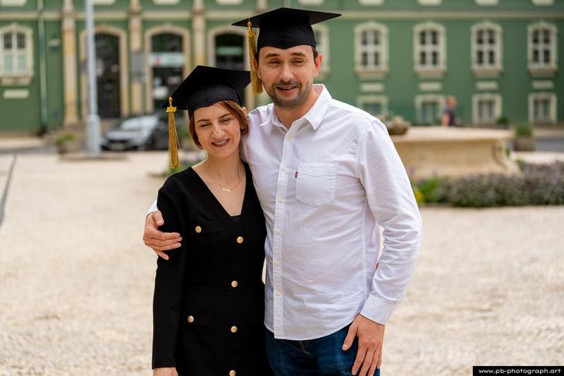 Reportaż z absolutorium w Szczecinie — uśmiechnięta para w togach na tle Urzędu Miasta.
