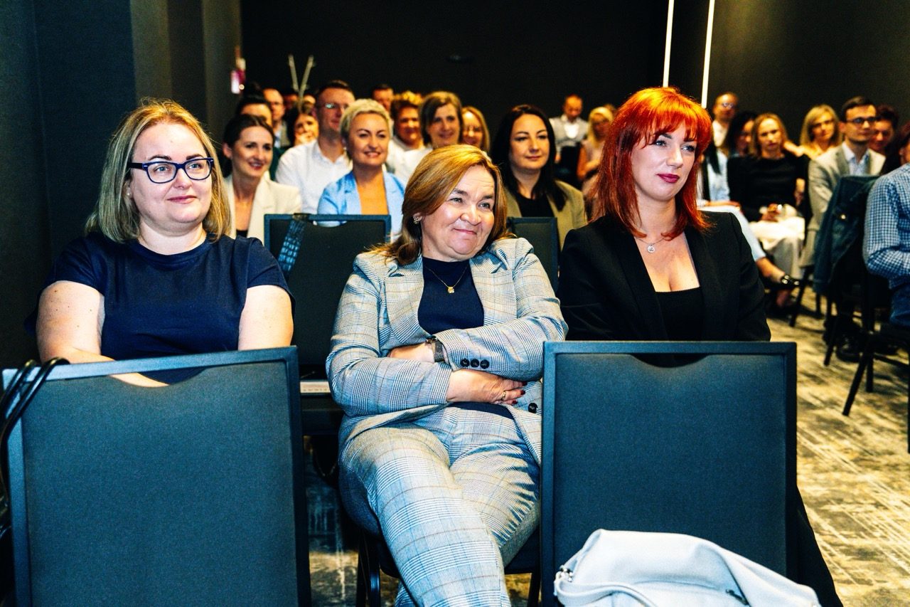 Uczestnicy wydarzenia siedzą na widowni i słuchają prezentacji
