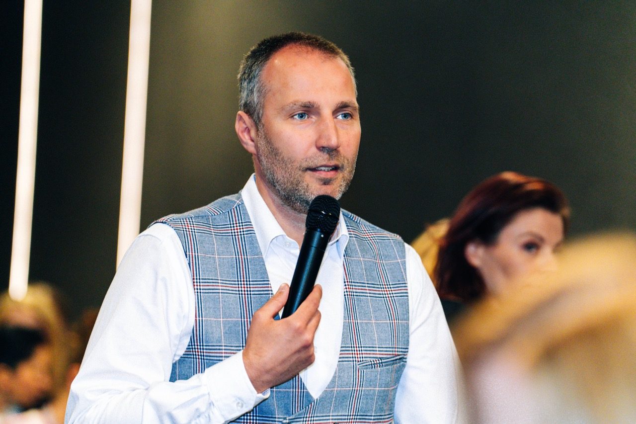Mężczyzna w kamizelce przemawia do mikrofonu podczas wydarzenia PKO