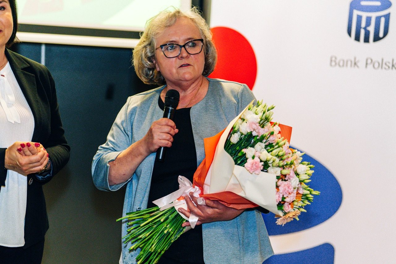 Kobieta z kwiatami i mikrofonem przemawia podczas rozdania wyróżnień PKO