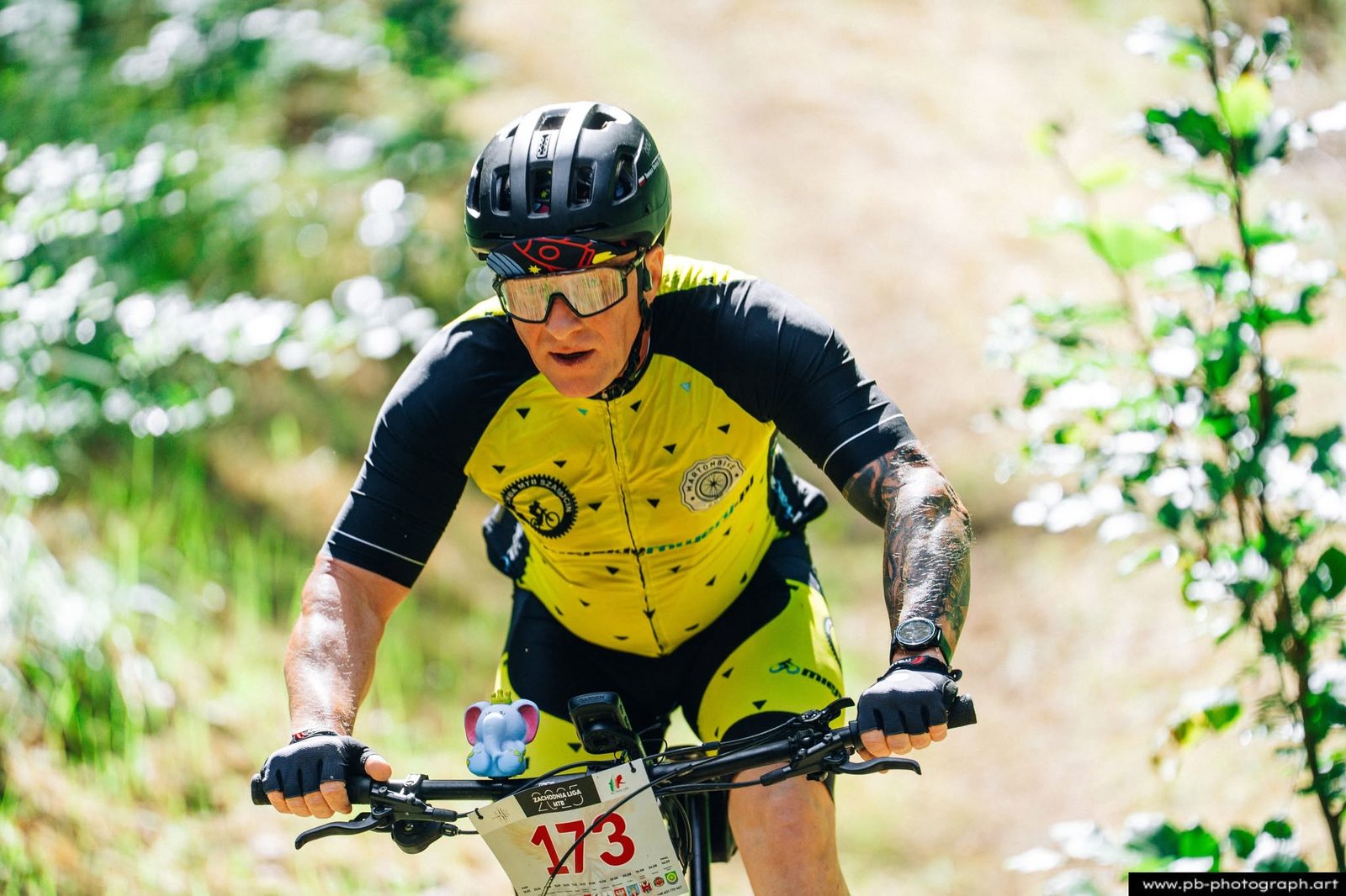 Zawodnik MTB w żółtym stroju jedzie rowerem przez leśną trasę wyścigu.