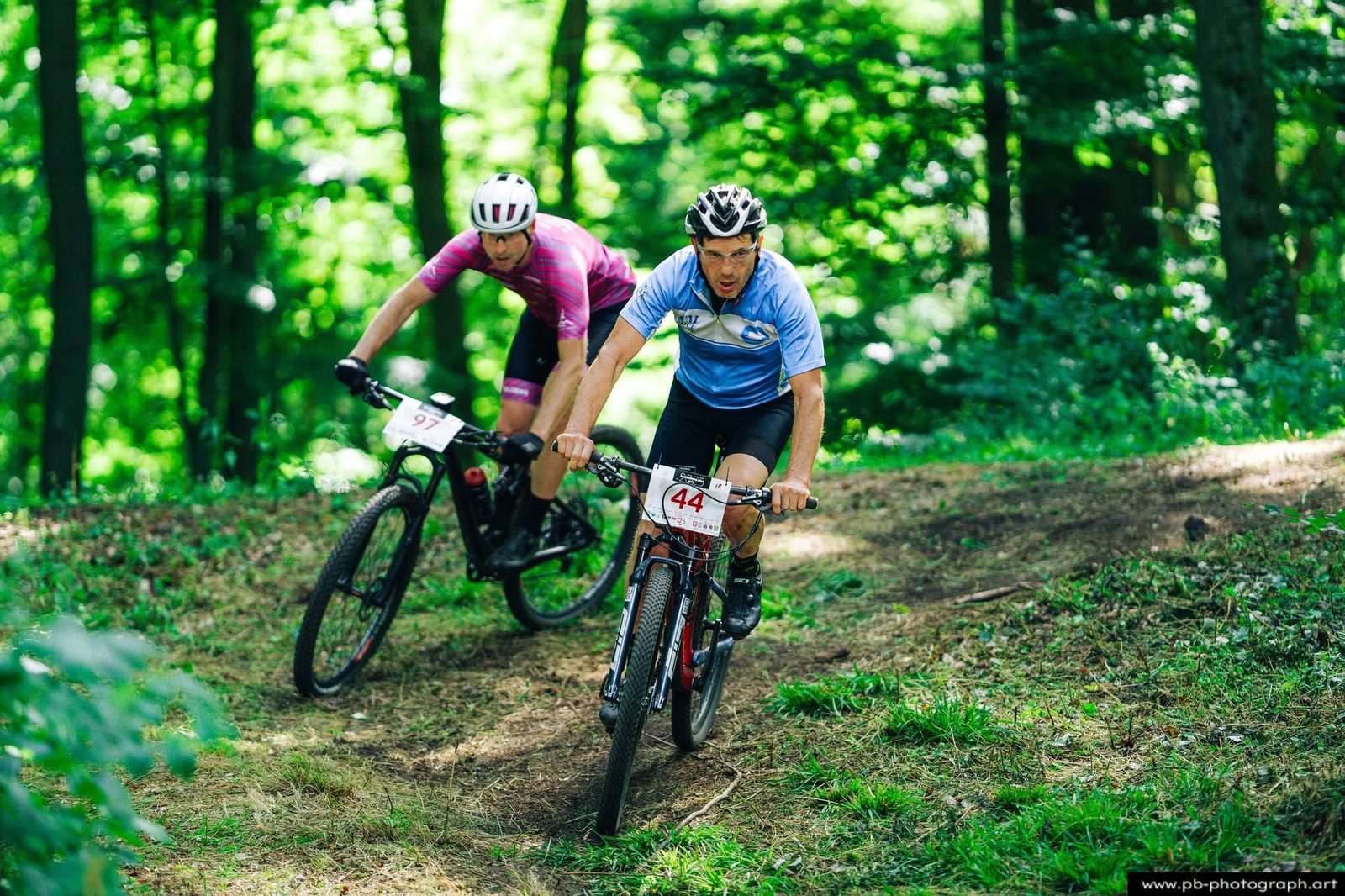Dwóch kolarzy MTB ściga się na zakręcie leśnej trasy podczas zawodów.
