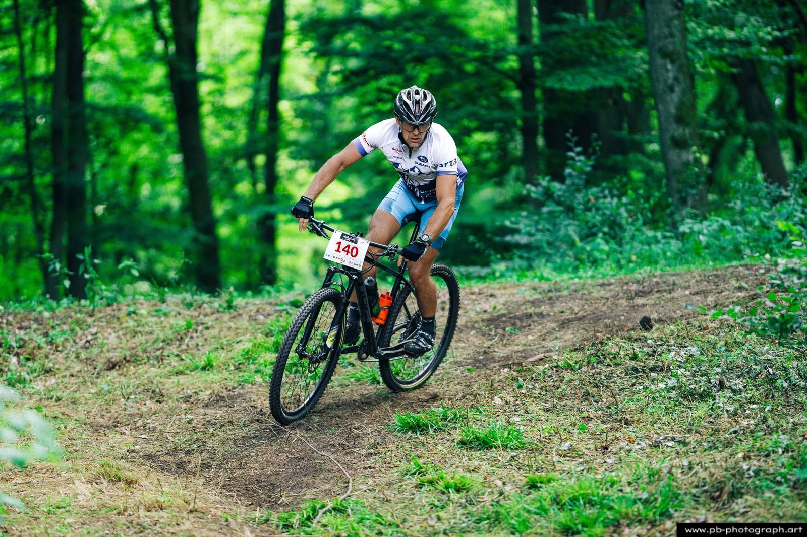 Zawodnik MTB w białym stroju skręca na leśnej ścieżce podczas wyścigu.