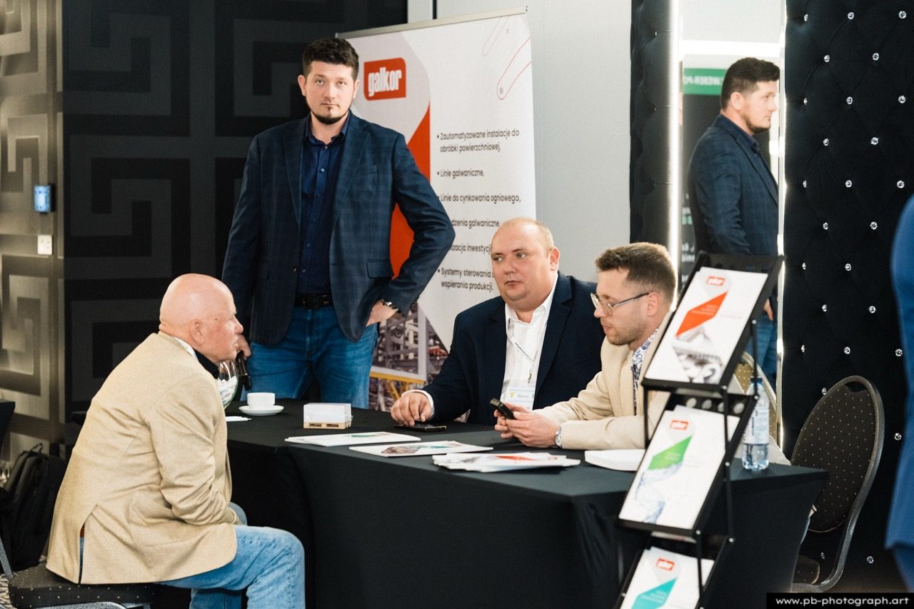 Grupa mężczyzn przy stole wystawowym na konferencji.
