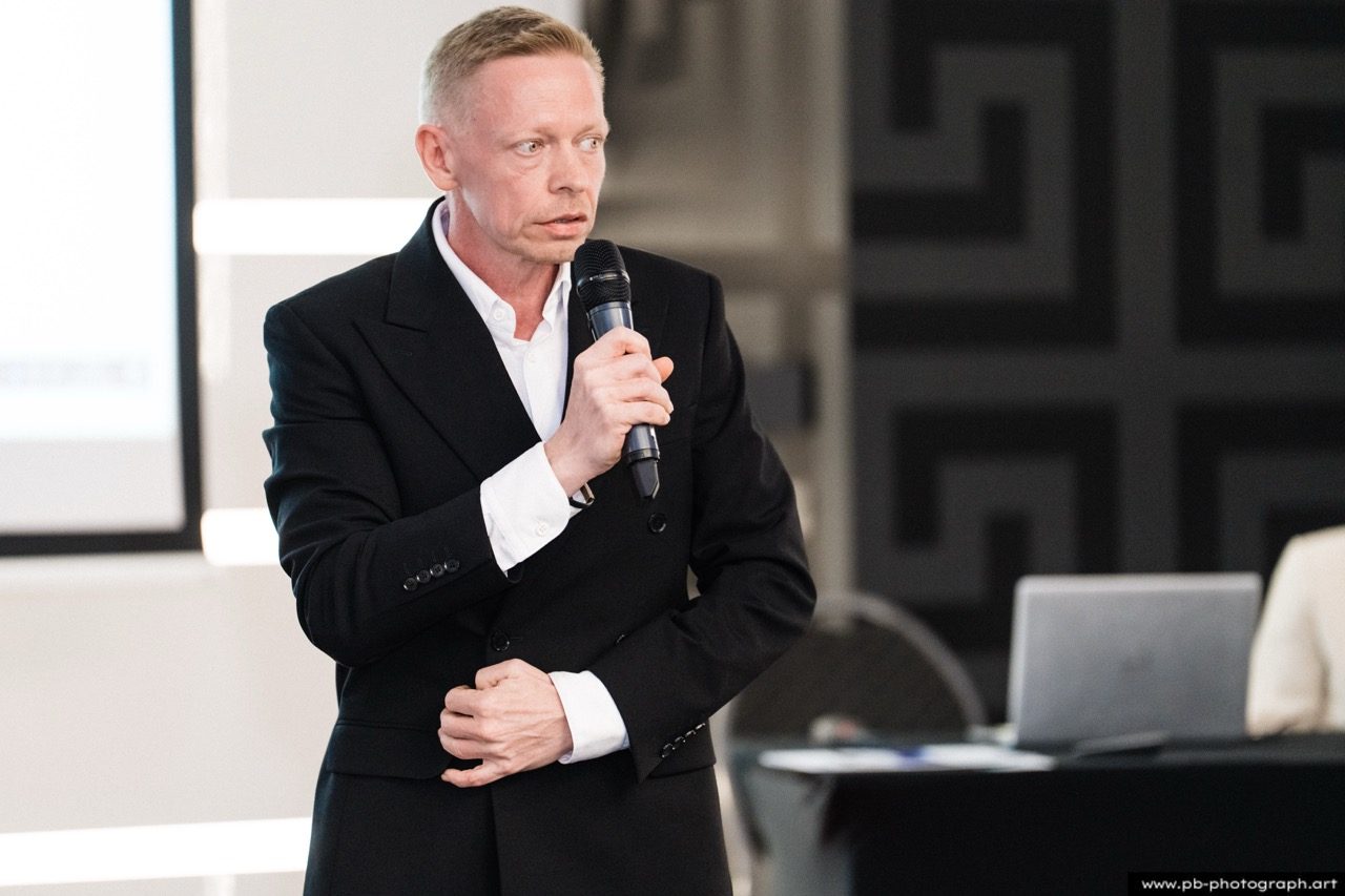 Mężczyzna w czarnym garniturze przemawia na konferencji.