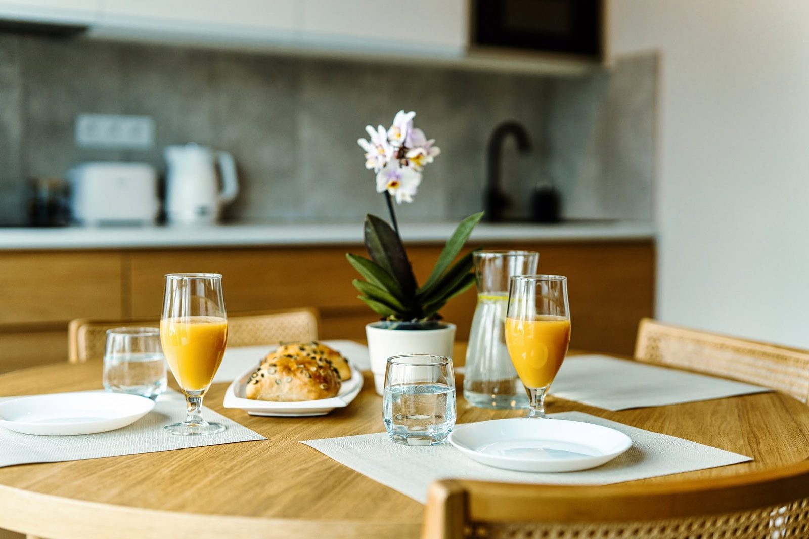 Stół z sokiem, pieczywem i kwiatem na tle kuchni w apartamencie